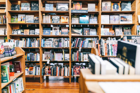A cozy bookstore interior with wooden shelves filled with various books and magazines. The shelves are packed tightly, displaying titles from different genres and topics, and the wooden floor adds warmth to the atmosphere.