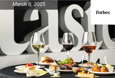 A selection of gourmet dishes and wine glasses on a black tablecloth, with plates of assorted appetizers and entrees. The background shows the word "Taste" in large letters.